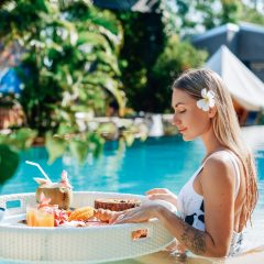 Female tourist in luxurious hotel enjoys swimming pool and tropical food